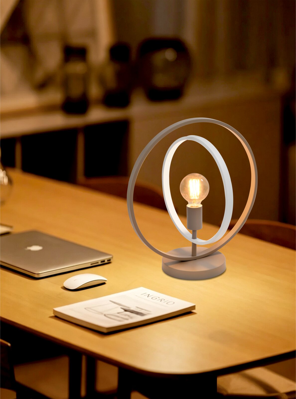 Moderne witte tafellamp met twee ovale ringen en een warme filamentlamp, schuin van voren gefotografeerd op een houten bureau in een sfeervol interieur.