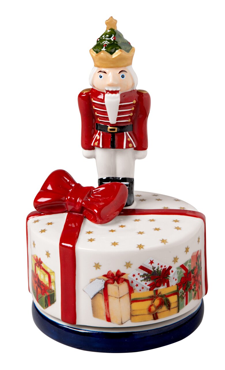 Spieluhr in Form eines Nussknackers auf einem runden, weihnachtlich verzierten Sockel mit Geschenkmotiven, aus der Frontalperspektive.