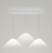 Moderne LED-Pendelleuchte mit drei zylindrischen Lampen, von der Seite betrachtet, die warmes Licht auf eine helle Wand projizieren.