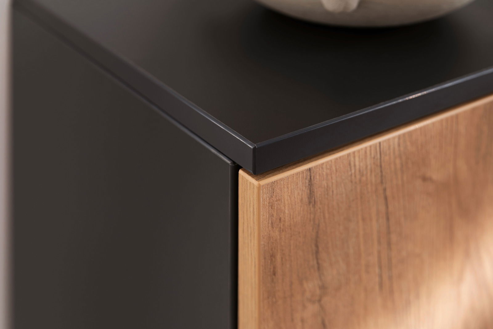 Nahaufnahme eines modernen Schuhschranks mit schwarzer Oberseite und Holzfront, Perspektive von oben.
