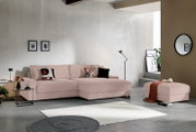 Modernes Ecksofa mit Chaiselongue in zartem Rosé/Beige aus geripptem Stoff, dekoriert mit gemusterten Kissen, im minimalistischen Wohnzimmer; Perspektive: frontale Ansicht leicht von links.