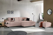 Modernes Ecksofa mit Chaiselongue in zartem Rosé/Beige aus geripptem Stoff, dekoriert mit gemusterten Kissen, im minimalistischen Wohnzimmer; Perspektive: frontale Ansicht leicht von links.