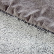 Nahaufnahme einer zweifarbigen Felldecke mit weicher, flauschiger Textur in Grau- und Beigetönen, von oben betrachtet.