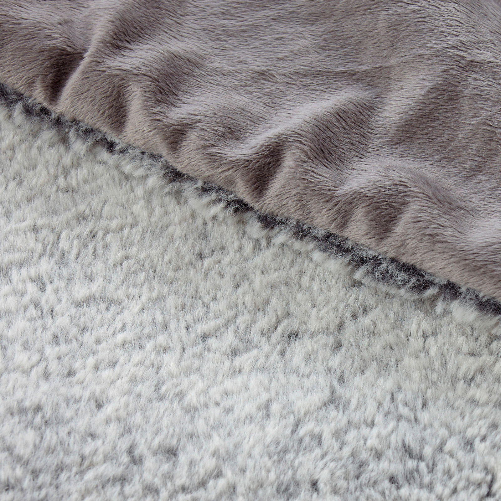 Nahaufnahme einer zweifarbigen Felldecke mit weicher, flauschiger Textur in Grau- und Beigetönen, von oben betrachtet.