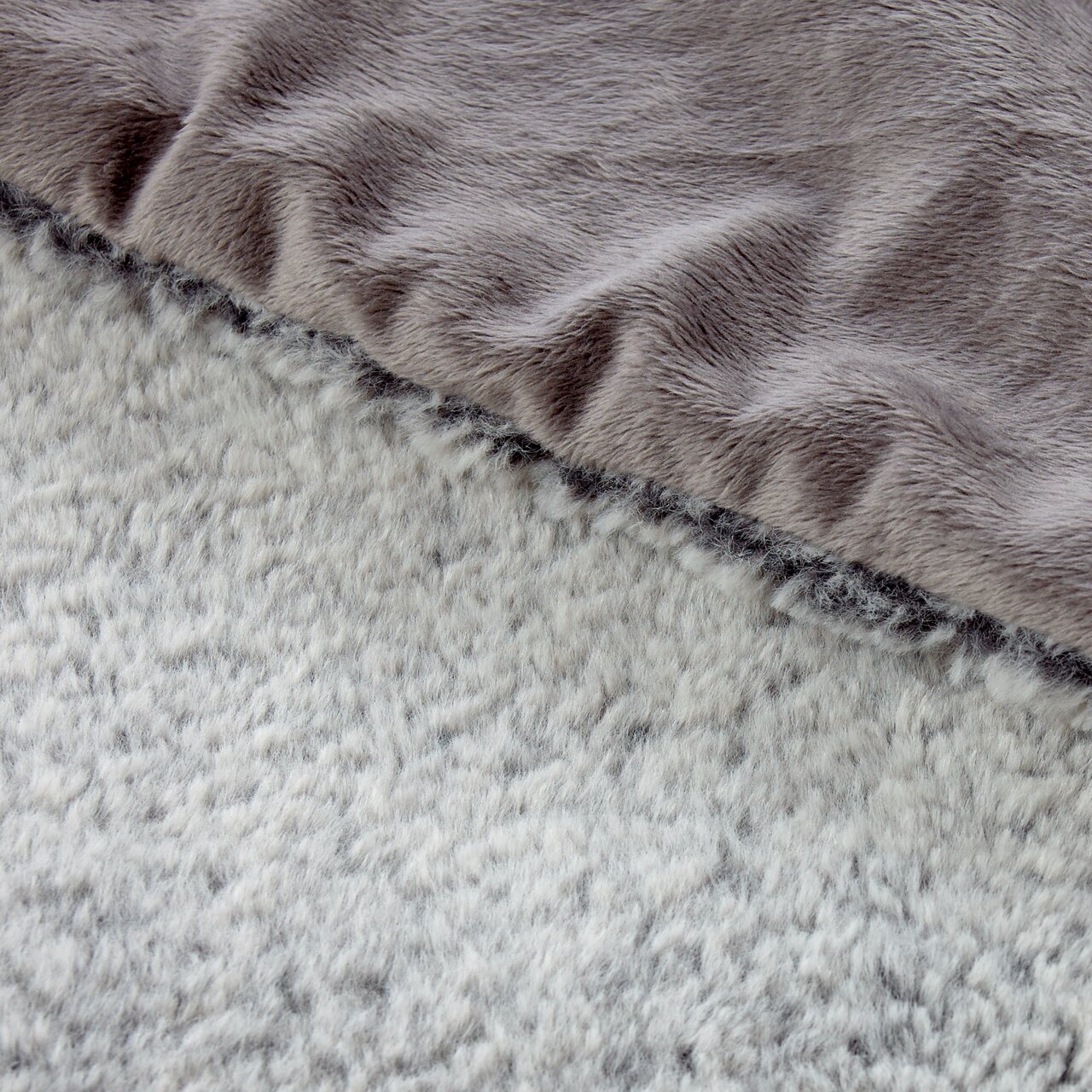 Close-up van een tweekleurige deken met een zachte, donzige textuur in grijze en beige tinten, gezien van bovenaf.