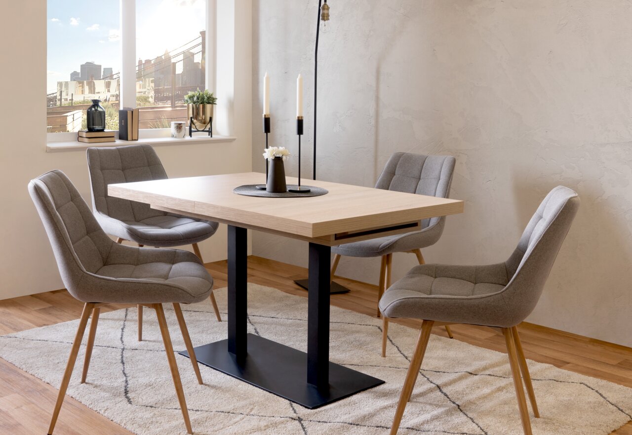 Moderner Esstisch mit hellem Holz und schwarzem Metallgestell, umgeben von vier grauen Polsterstühlen in einem hellen Raum mit Fenster im Hintergrund, seitliche Perspektive.