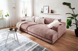 Gemütliches kleines Megasofa in einem modernen Wohnzimmer, seitliche Perspektive, mit weichen Kissen und einer Decke dekoriert.