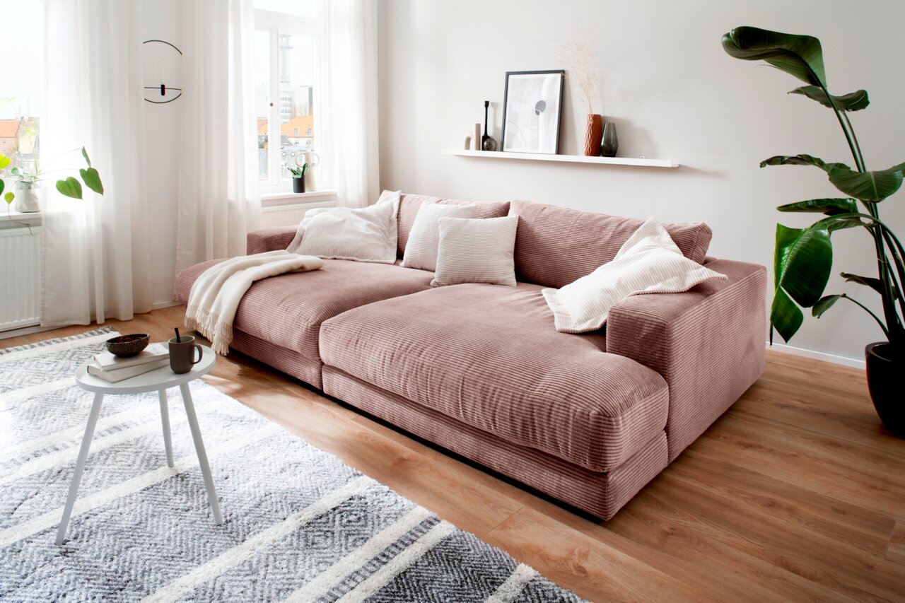 Gemütliches kleines Megasofa in einem modernen Wohnzimmer, seitliche Perspektive, mit weichen Kissen und einer Decke dekoriert.