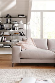 Beige Longchairkombination in einem modernen Wohnzimmer, seitliche Perspektive mit Bücherregal im Hintergrund.