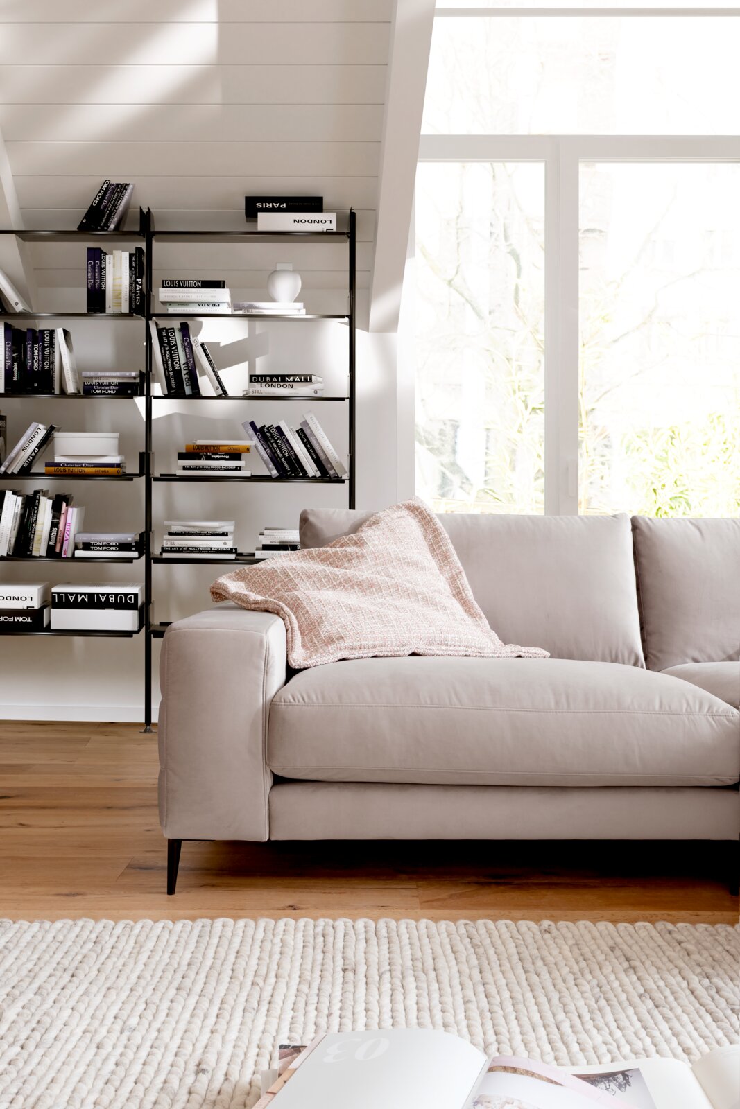 Beige Longchairkombination in einem modernen Wohnzimmer, seitliche Perspektive mit Bücherregal im Hintergrund.