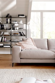 Beige Longchairkombination in einem modernen Wohnzimmer, seitliche Perspektive mit Bücherregal im Hintergrund.
