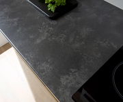 Draufsicht auf eine moderne, dunkle Küchenarbeitsplatte mit einem Kochfeld und einem Tablett mit grünen Kräutern.