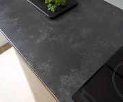 Draufsicht auf eine moderne, dunkle Küchenarbeitsplatte mit einem Kochfeld und einem Tablett mit grünen Kräutern.