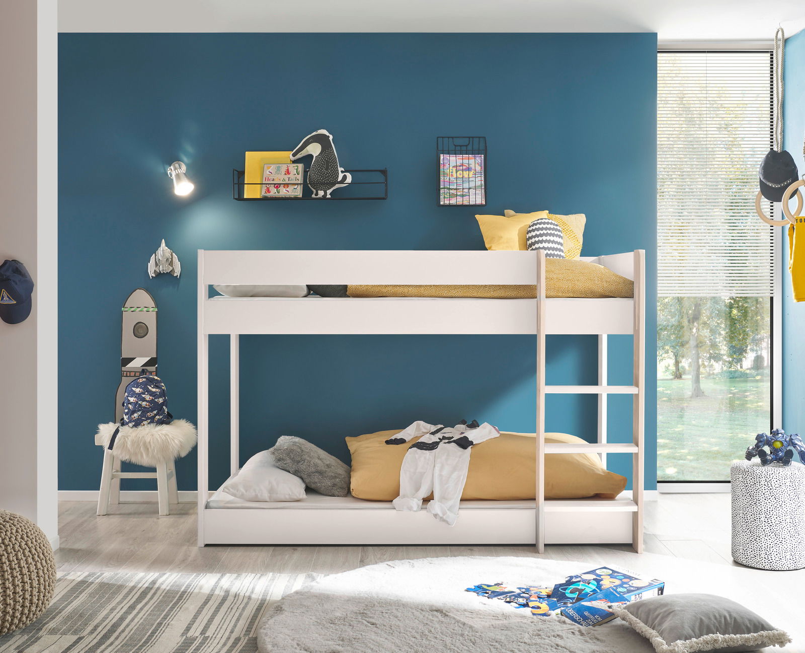 Weißes Etagenbett in einem modernen Kinderzimmer mit blauer Wand, dekoriert mit Spielzeug und Kissen, seitliche Perspektive.