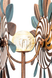 Nahaufnahme einer dekorativen Solarleuchte mit bronzefarbenen und blauen Metallblättern sowie einer gläsernen Kugel in der Mitte, aus seitlicher Perspektive.