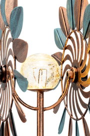 Close-up van een decoratieve zonne-lamp met bronskleurige en blauwe metalen blaadjes en een glazen bol in het midden, gezien vanaf de zijkant.
