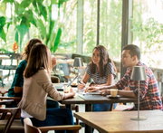 Akku-Tischleuchte COSENZA in einem modernen Café, seitliche Perspektive, umgeben von Menschen, die an einem Tisch arbeiten.