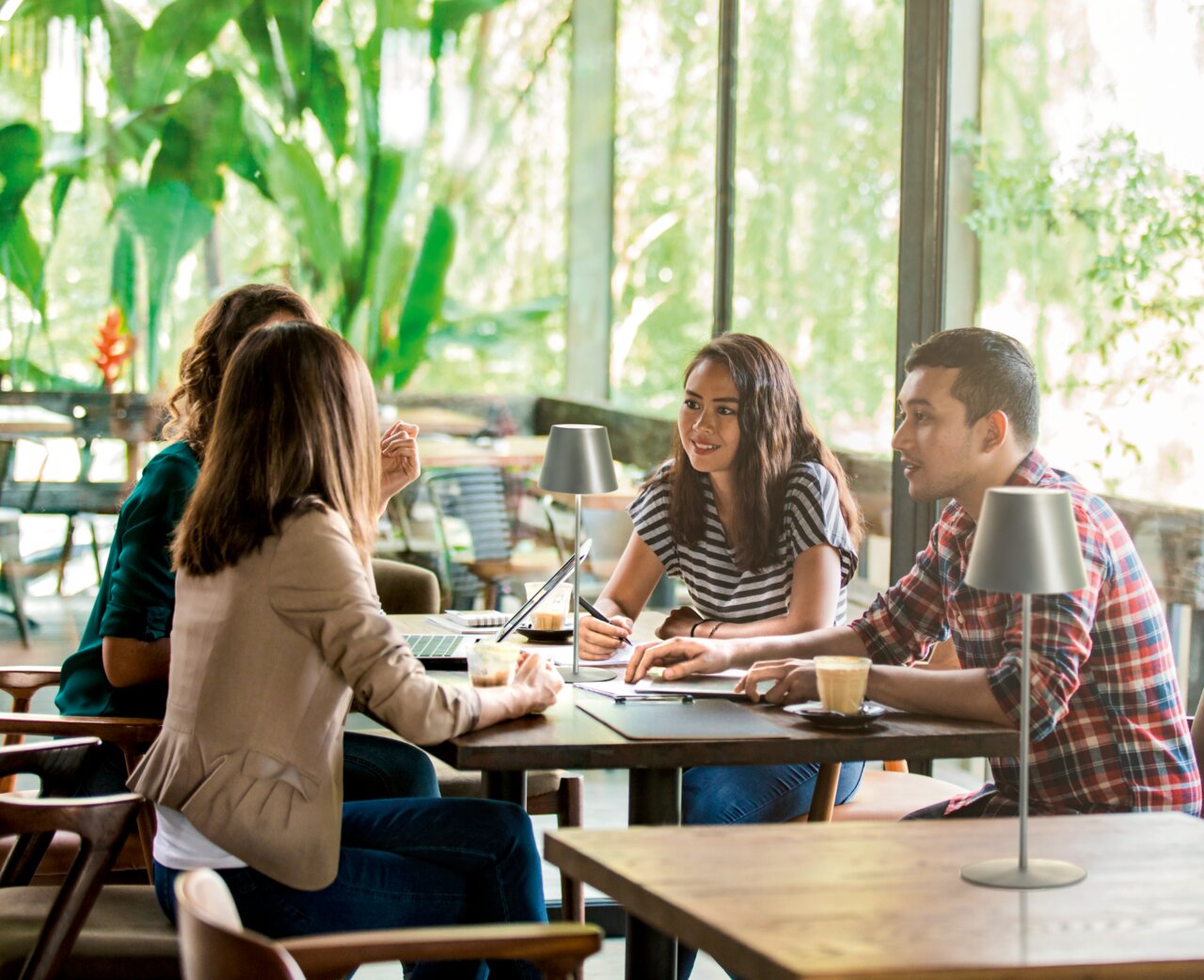 De COSENZA-tafellamp op accu in een modern café, gezien vanuit de zijkant, omringd door mensen die aan een tafel zitten te werken.