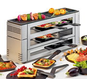 Silbernes Pizza-Raclette-Gerät mit mehreren Ebenen, gefüllt mit kleinen Pfännchen, die mit verschiedenen Zutaten belegt sind. Auf der oberen Grillfläche befinden sich Gemüse und Kartoffeln. Perspektive von der Seite.