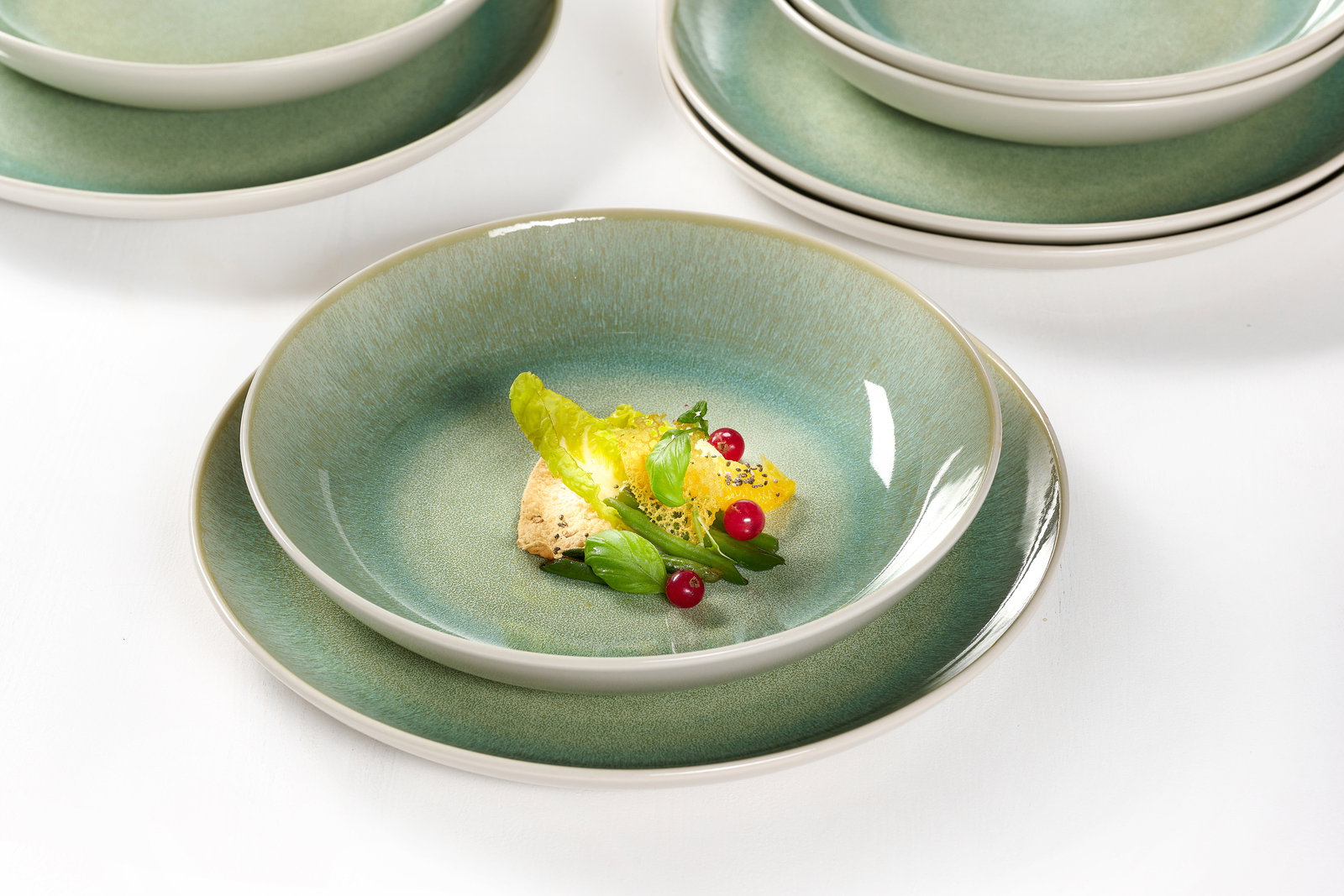 Nahaufnahme eines grünen Tafelsets mit elegantem Design, bestehend aus mehreren Tellern, auf einem weißen Hintergrund.