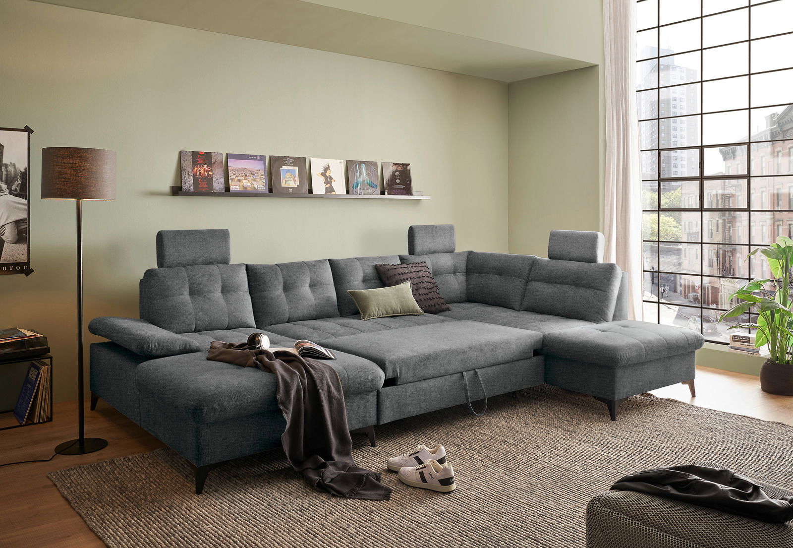 Graues Ecksofa in einem modernen Wohnzimmer, seitliche Perspektive mit Blick auf große Fenster und Dekoration.