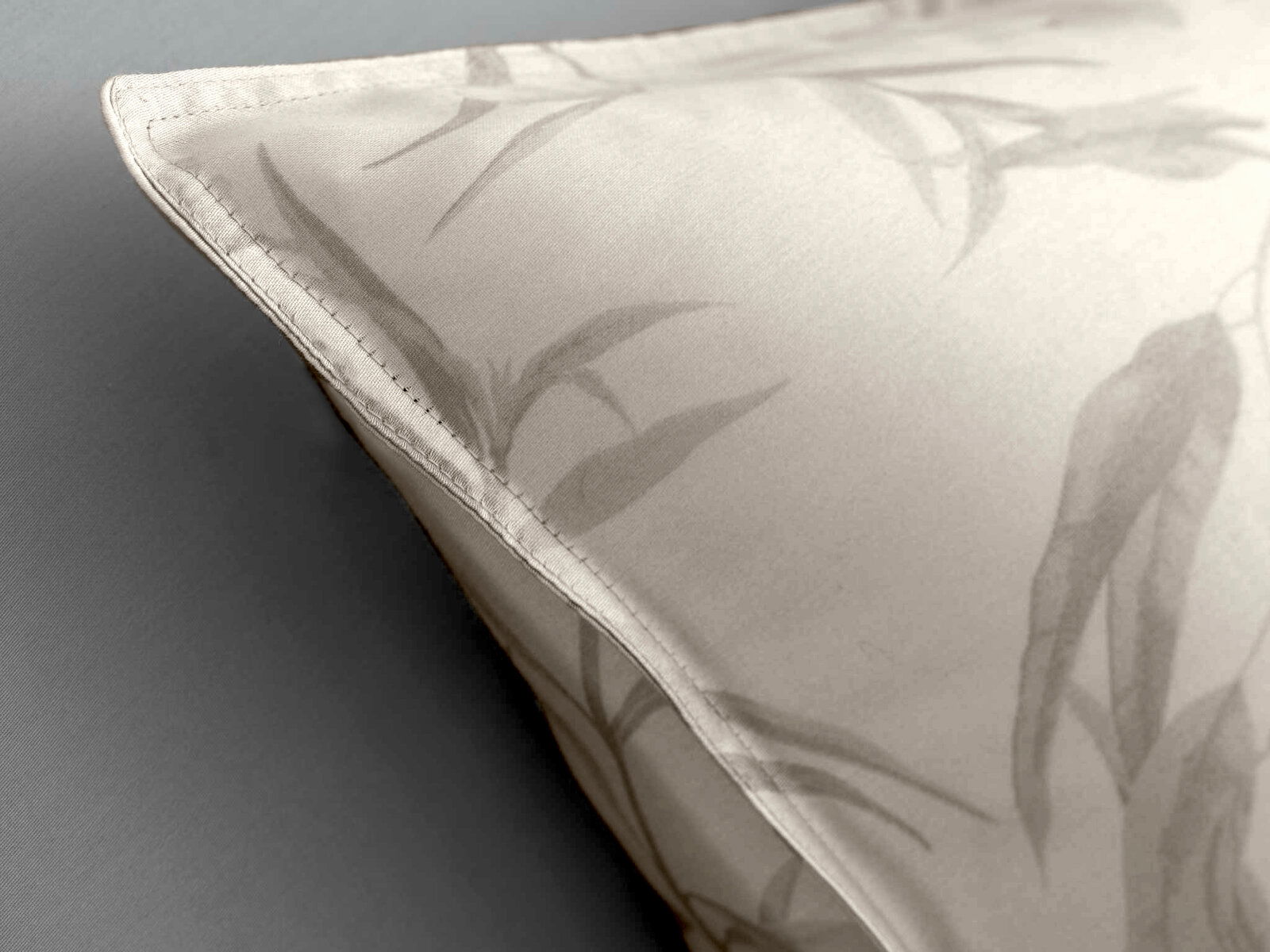 Nahaufnahme einer Bettwäsche mit floralem Muster in sanften Grautönen, perspektivisch von der Seite aufgenommen.