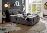 Gemütliches graues Boxspringbett in modernem Schlafzimmer mit Tageslicht, seitliche Perspektive