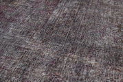 Close-up van een gestructureerd tapijt in verschillende grijstinten met een vleugje rood, schuin vanaf de zijkant gefotografeerd.