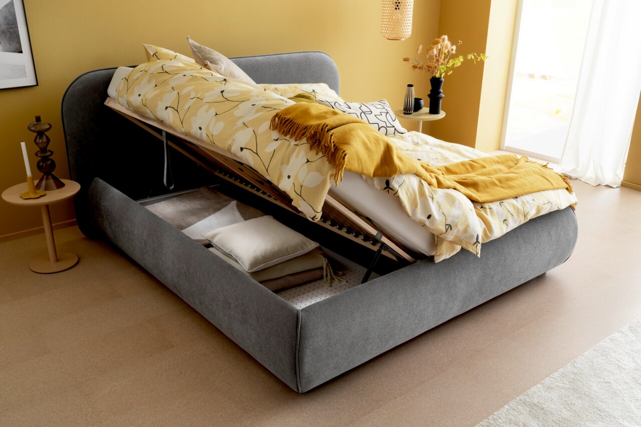 Graues Polsterbett mit hochgeklappter Matratze und Stauraum, seitliche Perspektive