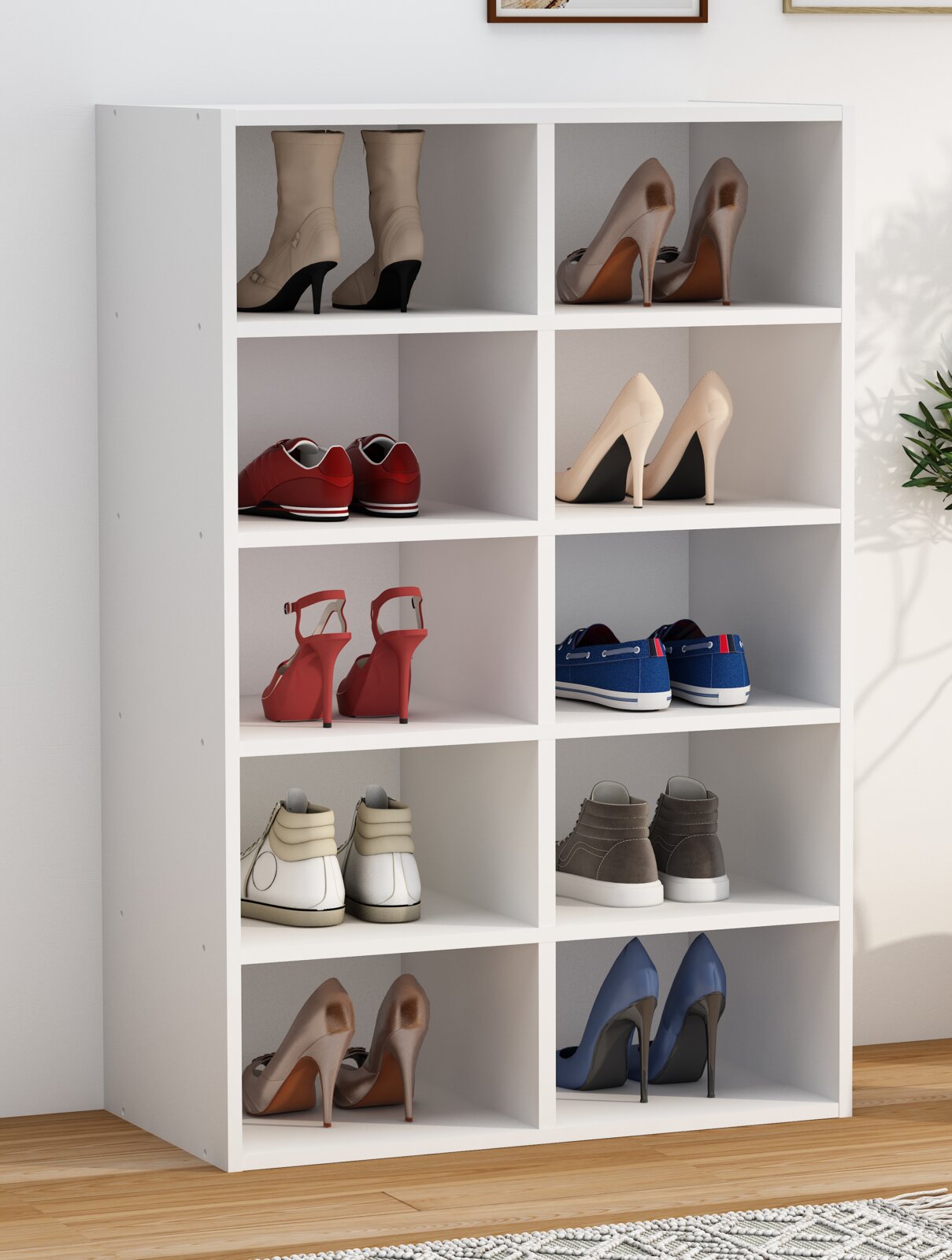 Weißes Schuhregal mit zehn Fächern, gefüllt mit verschiedenen Schuhpaaren (High Heels, Sneaker, Stiefeletten), in einem hellen Raum; Ansicht schräg von vorne.