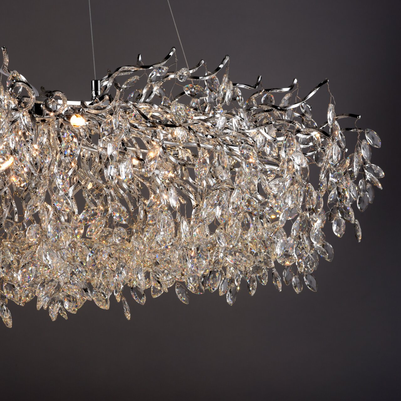 Nahaufnahme eines Kronleuchters RICICLE mit funkelnden Kristallen und silbernen Zweigen, seitliche Perspektive.