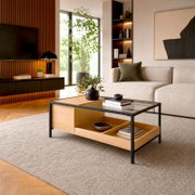 Moderner rechteckiger Couchtisch aus hellem Holz mit schwarzem Metallrahmen, Glasplatte und offenen Ablagefächern, aus schräger Vorderansicht in einem stilvollen Wohnzimmer präsentiert.