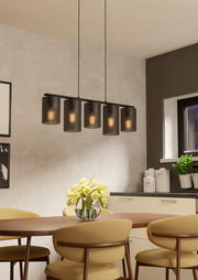 Moderne Pendelleuchte COLOMERA mit fünf zylindrischen, schwarzen Schirmen, hängend über einem Esstisch in einem stilvoll eingerichteten Raum, seitliche Perspektive.