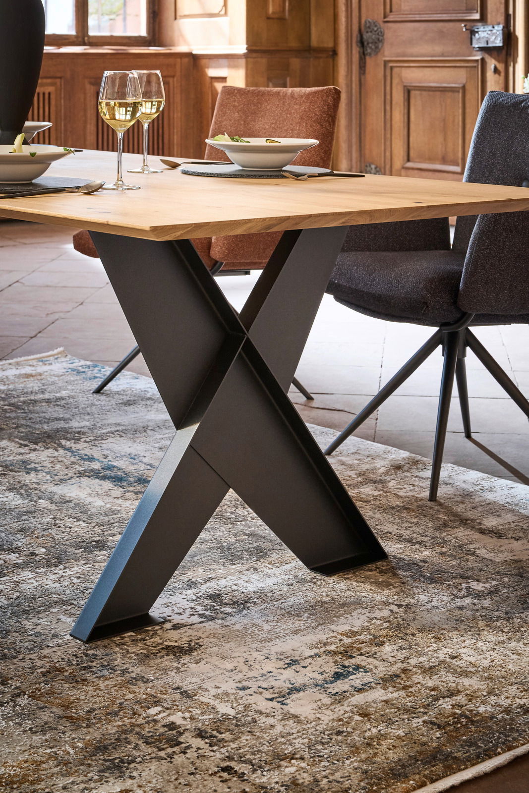 Moderner Esstisch mit Holzplatte und schwarzem Metallgestell in X-Form, seitliche Perspektive