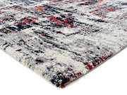 Nahaufnahme eines Designer-Teppichs mit abstraktem Muster in Grau, Rot und Blau, perspektivisch von der Seite aufgenommen.