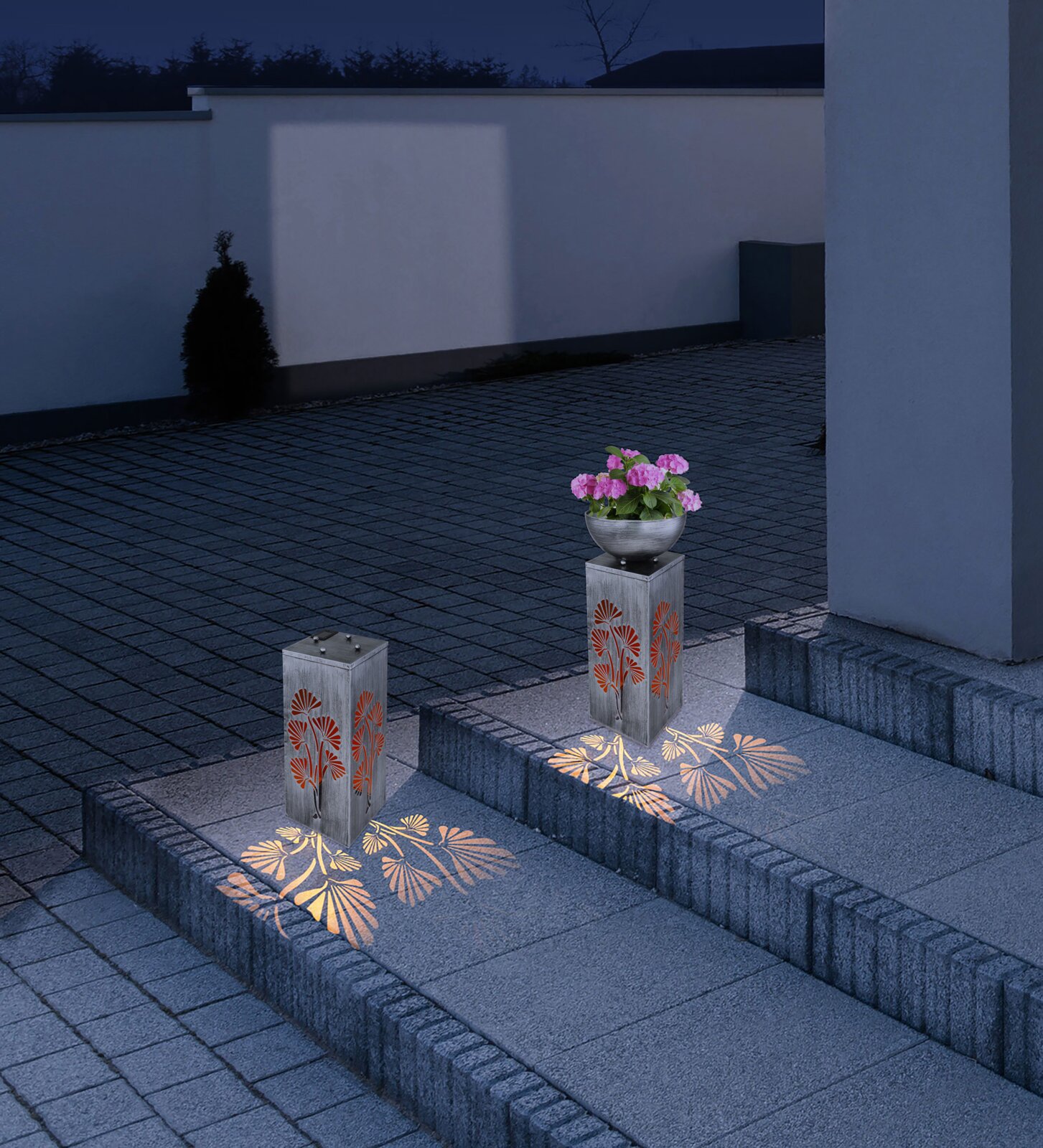 Solarleuchte mit floralem Muster, beleuchtet in der Nacht, auf einer Treppe platziert, seitliche Perspektive.