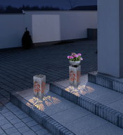 Solarleuchte mit floralem Muster, beleuchtet in der Nacht, auf einer Treppe platziert, seitliche Perspektive.