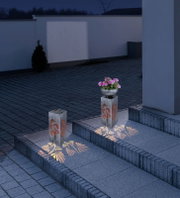 Solarleuchte mit floralem Muster, beleuchtet in der Nacht, auf einer Treppe platziert, seitliche Perspektive.