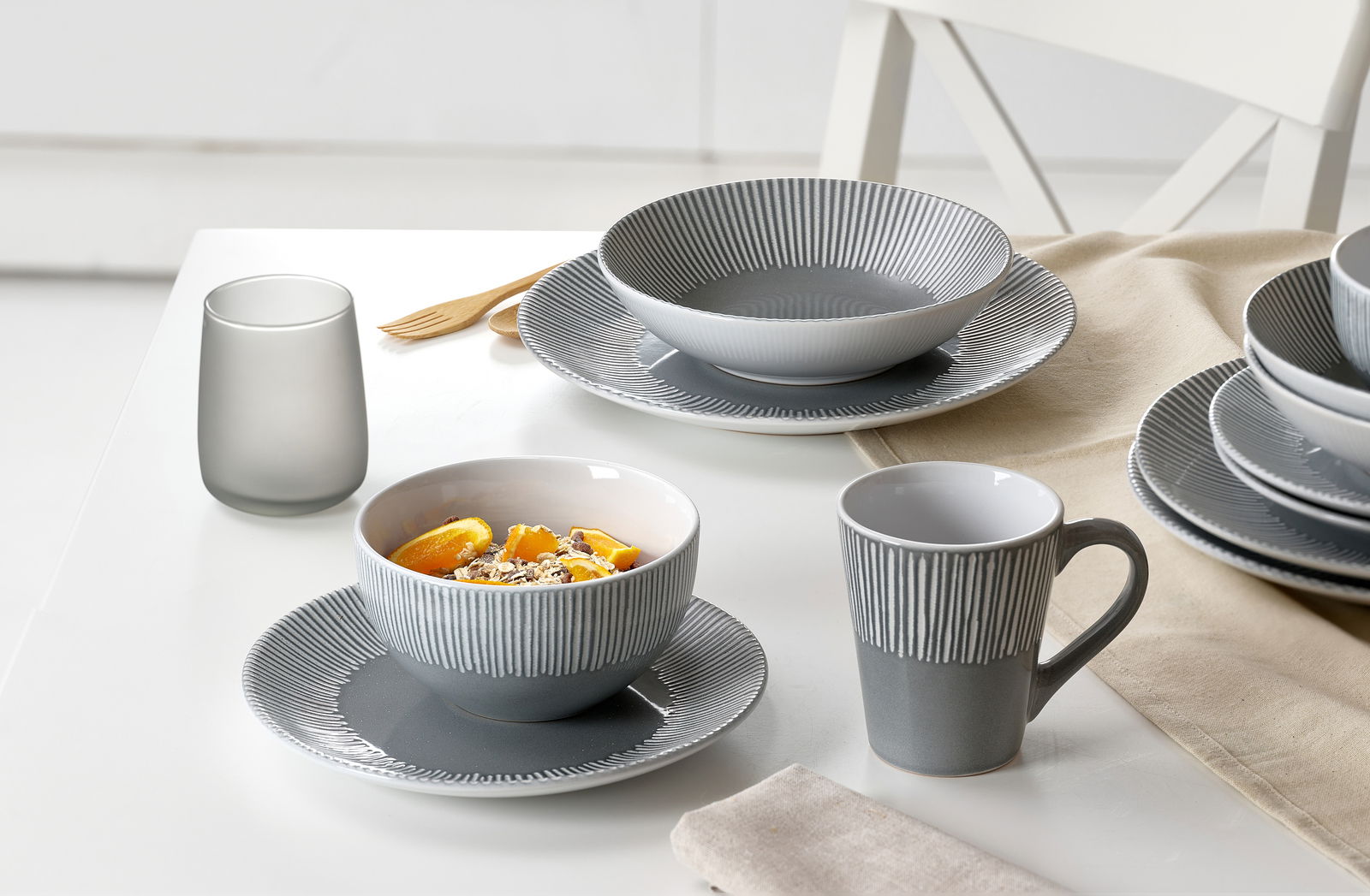Ritzenhoff & Breker Tellerset 18-tlg. BANDA Graues 18-teiliges Tellerset mit modernem Streifenmuster, bestehend aus Tellern, Schalen und Tassen, auf einem Tisch arrangiert. Perspektive von schräg oben.