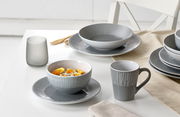 Graues 18-teiliges Tellerset mit modernem Streifenmuster, bestehend aus Tellern, Schalen und Tassen, auf einem Tisch arrangiert. Perspektive von schräg oben.
