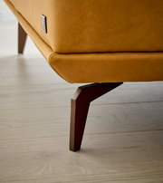 Nahaufnahme eines Longchairs mit braunem Lederbezug und modernen Holzbeinen, seitliche Perspektive.