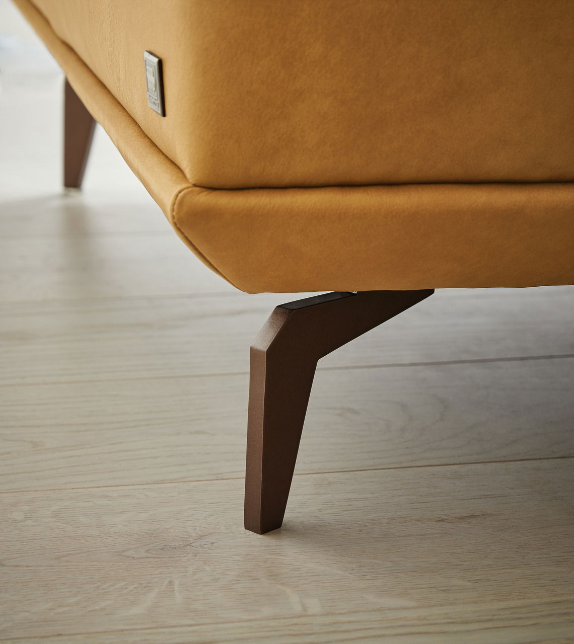 Nahaufnahme eines Longchairs mit braunem Lederbezug und modernen Holzbeinen, seitliche Perspektive.