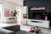 Modernes Wohnzimmer mit weißer Wohnwand (TV-Lowboard, Hängeregal und Vitrine) mit Holz-Akzenten vor dunkler Wand, frontal in leichter Weitwinkelperspektive aufgenommen