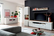 Modernes Wohnzimmer mit weißer Wohnwand (TV-Lowboard, Hängeregal und Vitrine) mit Holz-Akzenten vor dunkler Wand, frontal in leichter Weitwinkelperspektive aufgenommen