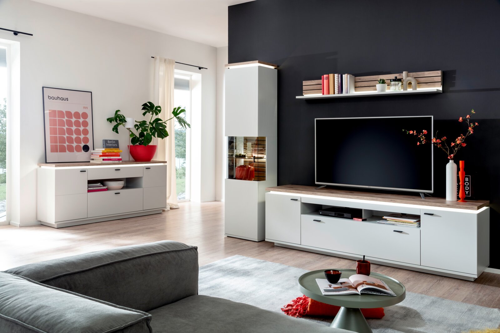 Stylife Sideboard ESTEPONA Modernes Wohnzimmer mit weißer Wohnwand (TV-Lowboard, Hängeregal und Vitrine) mit Holz-Akzenten vor dunkler Wand, frontal in leichter Weitwinkelperspektive aufgenommen