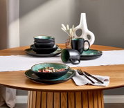 Kombiservice 10-teilig in Schwarz und Grün auf einem Holztisch, bestehend aus Tellern, Schalen und Tassen, seitliche Perspektive.