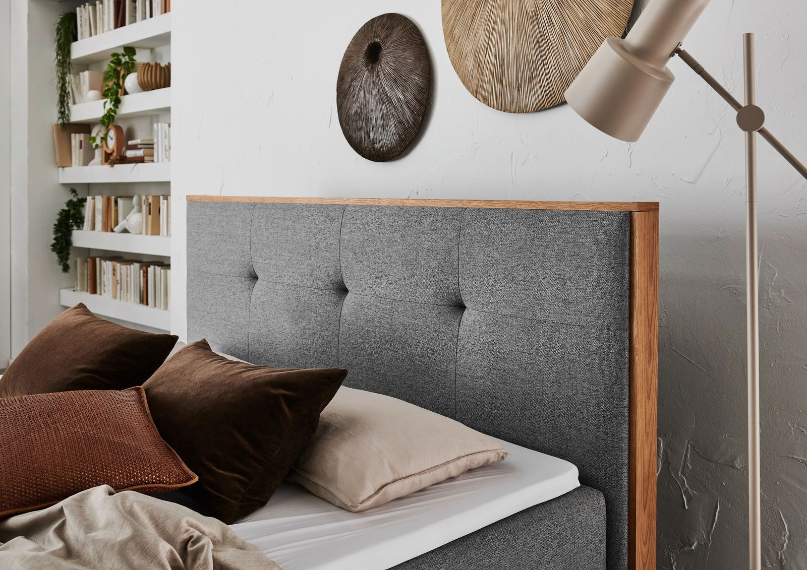 Graues Boxbett mit Holzrahmen, dekoriert mit braunen Kissen, seitliche Perspektive
