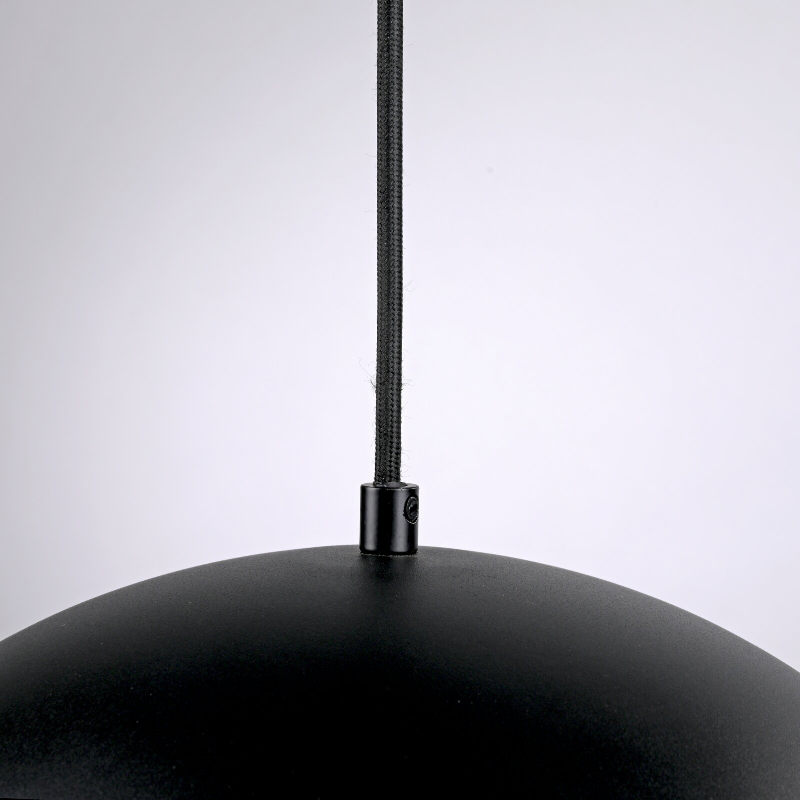 Detailaufnahme einer schwarzen Pendelleuchte mit textilummanteltem Kabel und Metallhalterung am Lampenschirm, frontale Nahansicht von oben