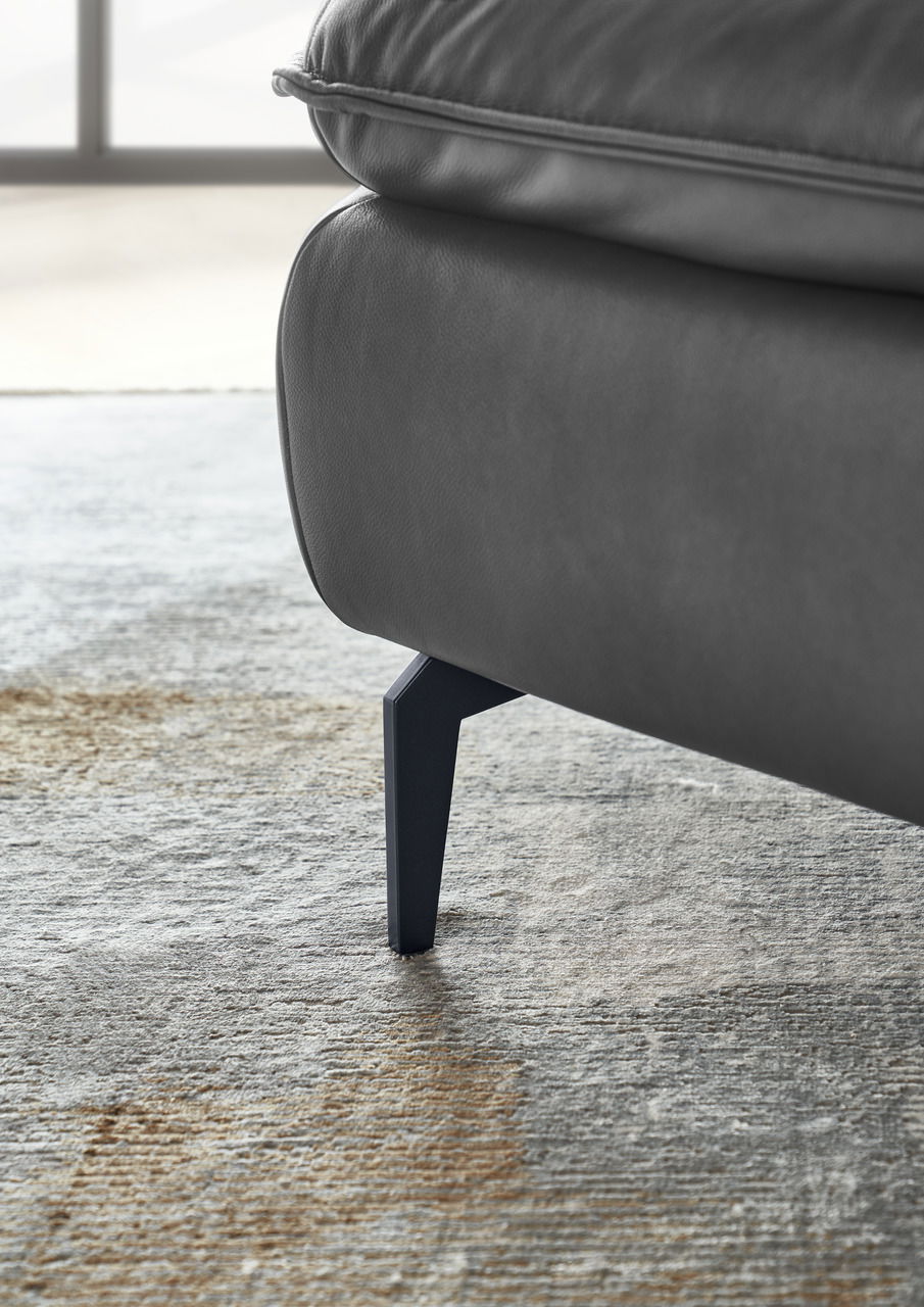 Nahaufnahme eines grauen Sofas mit Metallbeinen auf einem Teppich, seitliche Perspektive.
