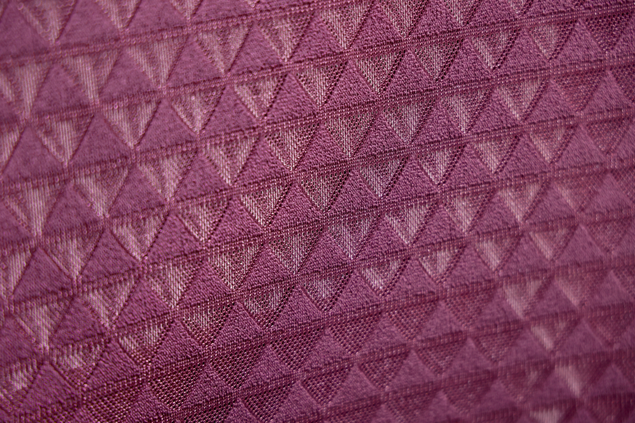 Nahaufnahme eines lila Stoffes mit dreieckigem Muster, perspektivisch von der Seite aufgenommen.